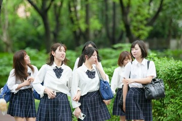 In early June in Pudong, Shanghai, seven Japanese high school girls wearing summer uniforms are walking to school along a lush green street, surrounded by vibrant foliage and early summer sunlight.