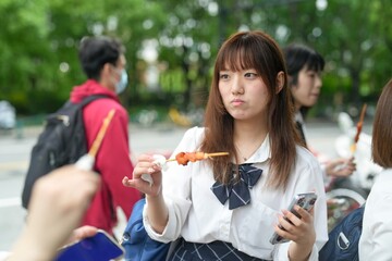 In early June in Pudong, Shanghai, seven Japanese high school girls in summer uniforms gather at a local street food stall, enjoying skewered meat and chatting before heading off to school together.