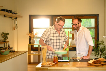 Smiling father and adult son preparing a pasta meal together in a cozy home kitchen. Father day concept