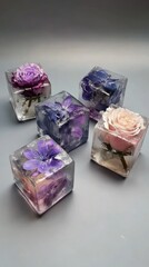 Five small, clear cubes, each encasing a different preserved flower in shades of purple, pink, and blue, sit on a gray surface