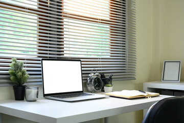 Minimalist home office setup with a laptop, notebook, and alarm clock near a window