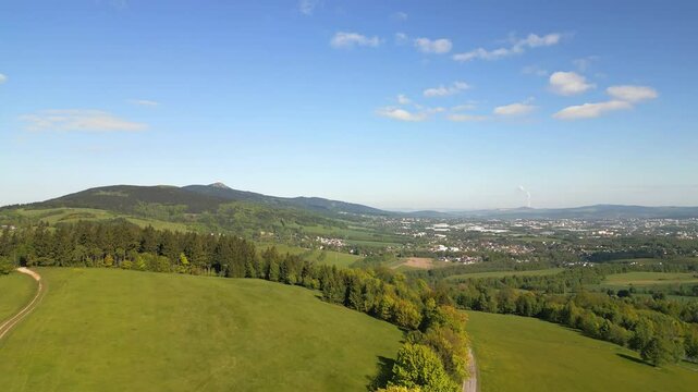 Aerial view from drone of lush meadows, rolling hills and the iconic Jested Mountain in the distance, with the city of Liberec visible on the horizon