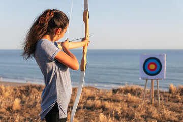 Archeress aiming at target with bow and arrow at beach