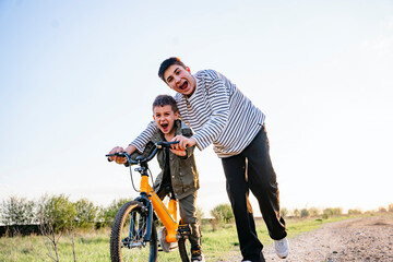 Teen teaching younger brother how to ride a bicycle outdoors at sunset