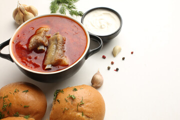 Traditional Ukrian food borscht with sour cream in a clay pot with bread, garlic, buryak tomatoes and greens