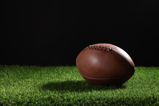 A textured American football resting on the green artificial turf with white line. College Football