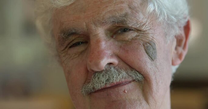 Close-up of an elderly man with a teasing expression, winking and blowing kisses as if flirting with someone off-camera