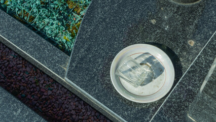 A granite gravestone with a plate and an overturned empty shot glass symbolizes remembrance of deceased relatives. A tribute to family traditions, loss, and honoring loved ones at the cemetery.