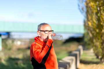 Senior man drinking water after outdoor exercise in nature