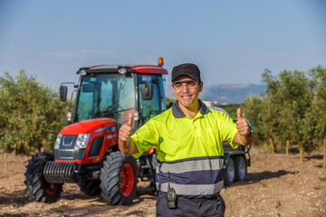 Farmer with tractor showing thumbs up in olive grove under clear sky