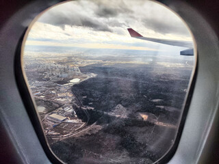 Fototapeta premium View from airplane window showcasing landscape and clouds during a flight over urban and rural areas