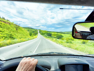 Driving along a scenic road surrounded by lush greenery on a partly cloudy day