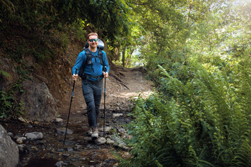 Hiker with backpack walking along forest trail through mountain stream.
