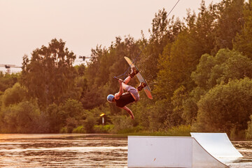 Wakeboarder making tricks. Low angle shot of man wakeboarding on a lake. Man water skiing at sunset.	