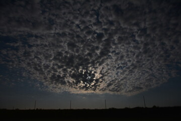 A dramatic night sky is covered with a thick blanket of textured altocumulus clouds, with the moon partially visible through a clearing.