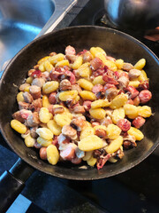 Homemade dish with gnocchi, bacon, sausages, mushrooms and cheese on a frying pan