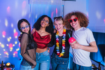 Four cheerful multi ethnic friends enjoying a house party with colorful disco lights, hugging and smiling
