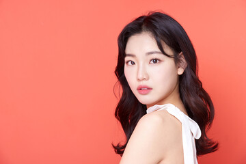 Young Asian Woman with Wavy Hair in White Sleeveless Top on Coral Background
