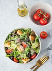 Salad with lettuce, tomatoes, croutons, olives and parmesan cheese in a bowl on a light background