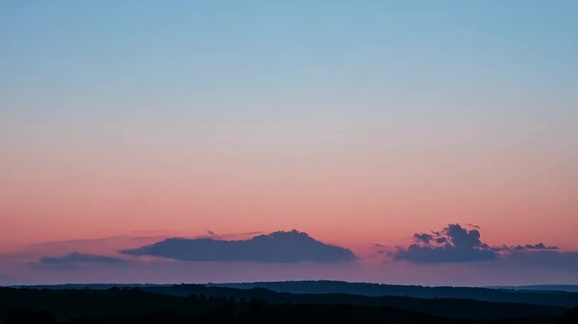 Peaceful sunset sky with soft pink and blue gradient above distant hills, calm evening landscape scene