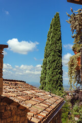 Beautiful view of Assisi with ancient rooftops and cypress trees under a bright blue sky in Umbria, Italy