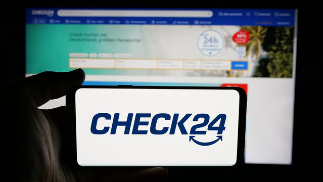 Stuttgart, Germany - 05-25-2025: Person holding cellphone with logo of German price comparison company Check24 GmbH on screen in front of webpage. Focus on phone display.