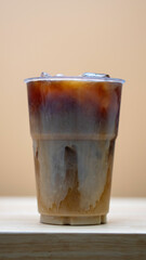 plastic cup filled with iced coffee shows a beautiful swirl of milk blending into the dark brew.