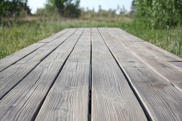 A long, grey wooden boardwalk extends into a blurry green field, vanishing point perspective
