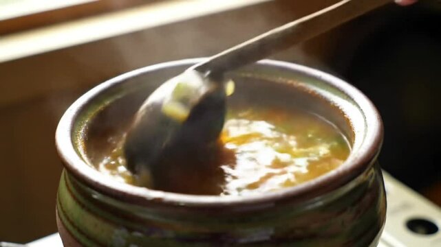 A steaming pot of soup being stirred, evoking warmth and comfort.