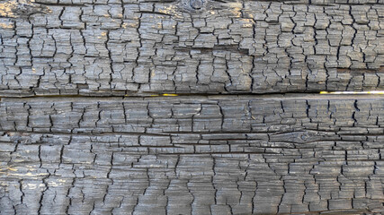 Detailed close-up of burned wooden boards with deep cracks and charred surface texture, perfect for disaster themes, fire aftermath visuals, or rustic natural backgrounds