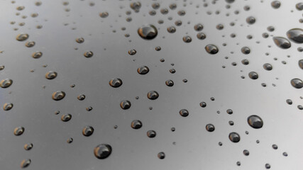 High-resolution macro of round water droplets scattered across dark smooth surface, creating dramatic pattern and reflective highlights perfect for abstract backgrounds and texture overlays
