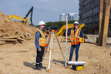 Two construction surveyors in safety gear perform land measurement at a worksite using a total...