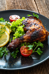 Oven roasted chicken leg with lemon and greens on wooden table	