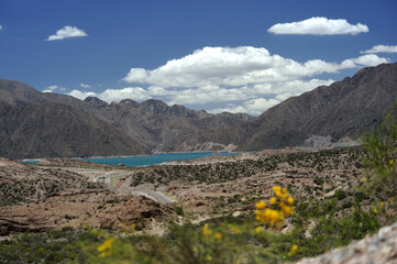 A magnificent photo with a blue lake, cloudy sky, semi-desert, and a road between the mountains
