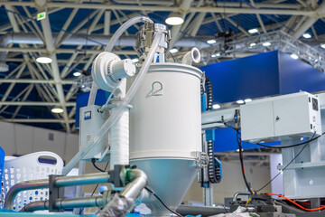 Industrial plastic granule tank with attached hoses and metal components in factory environment. Plastic injection molding production line