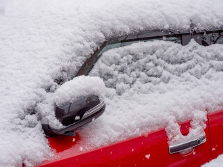 Snow-covered red car door and side mirror in close-up photography style on outdoor background....