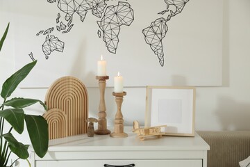 Stylish candlesticks with burning candles and other decor on cabinet near wall indoors