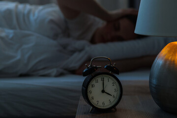Frustrated young woman suffering from insomnia on bed indoors, focus on alarm clock