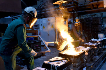 Group of workers in an iron foundry - casting a workpiece with liquid hot metal into a mold - cooperation and work safety