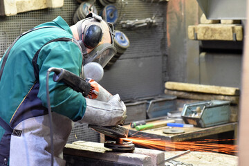 Worker with a grinding machine machines a workpiece made of steel in an industrial company - work safety with ear and eye protection