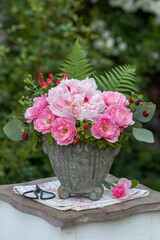 Blumen-Arrangement mit pink Pfingstrose und Rosen im vintage Blumentopf im Garten