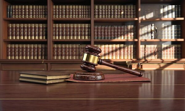 A wooden gavel rests on a red mat in a law office, surrounded by law books on shelves