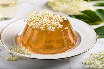 Holundergelee, hollerblütengelee, in Puddingform, auf einem weißen Teller  und mit einzelne Blüten dekoriert