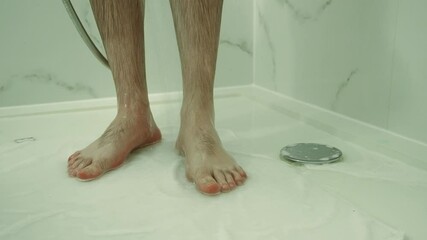 Man washing feet in hotel shower while standing on towel. Practicing hygiene to avoid fungal infections. Rinsing legs carefully in tiled bathroom. Taking health precautions during morning shower