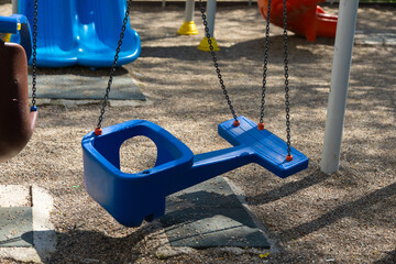 Close-up of a blue plastic toddler swing with safety backrest, suspended by chains on a...