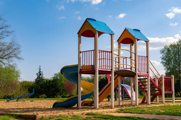 Vibrant children’s playground with slides, stairs, and sandy ground in a park setting on a sunny...