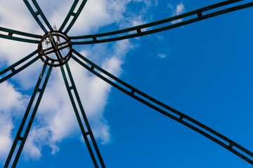 Weathered metal structure viewed from below, radiating outward from a central ring against a vivid...