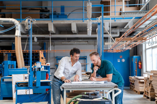 Two carpenters talking over documents in production hall