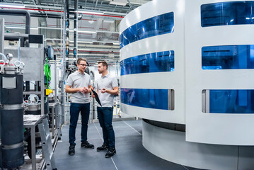 Two employees discussing in a modern production hall with machinery