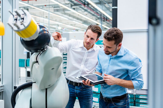 Employees discussing in a production hall with an industrial robot and a tablet